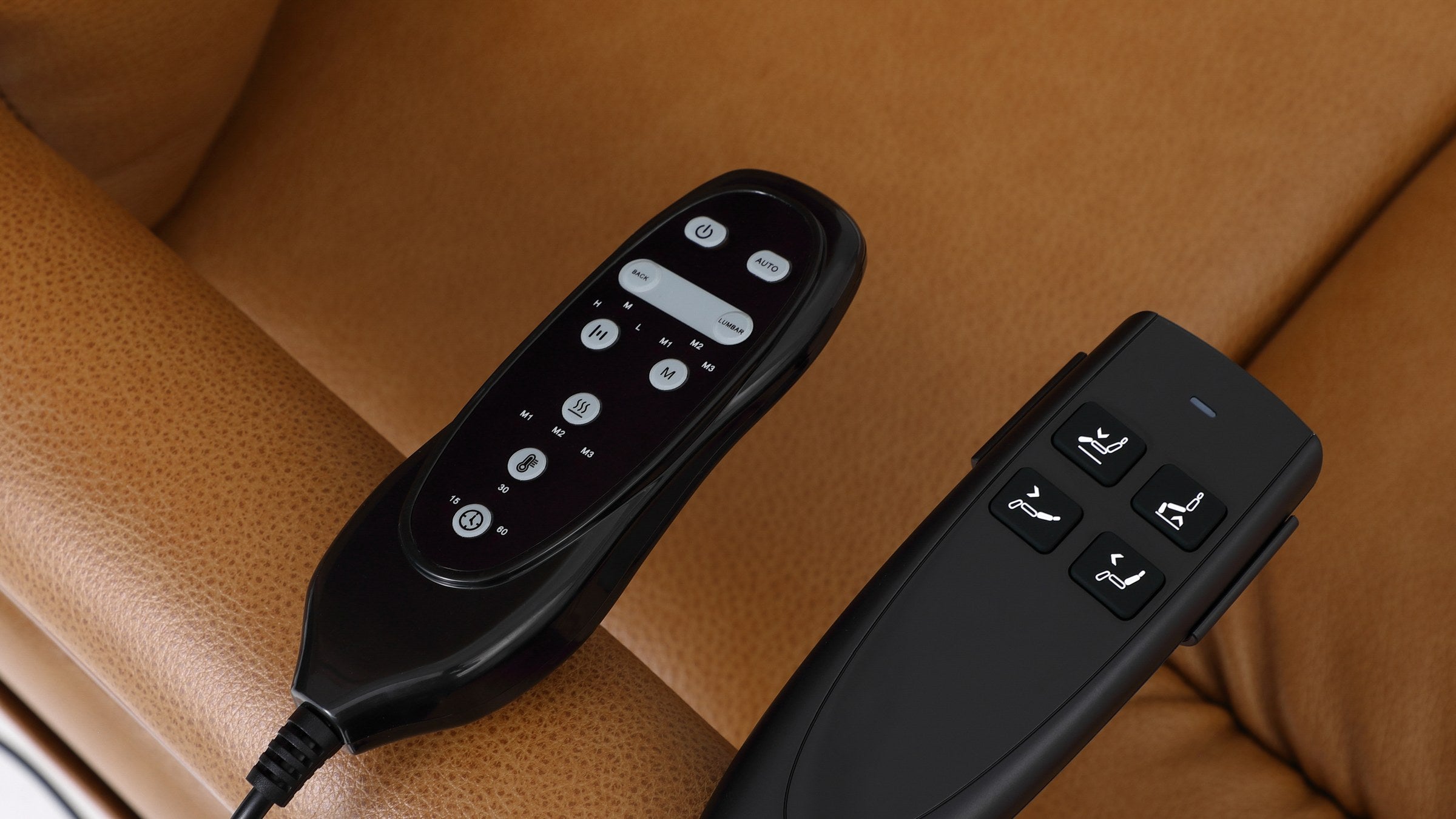 The two Irene House 9185 hand controls resting on the camel brown leather seat: the position handset and the heat and massage handset