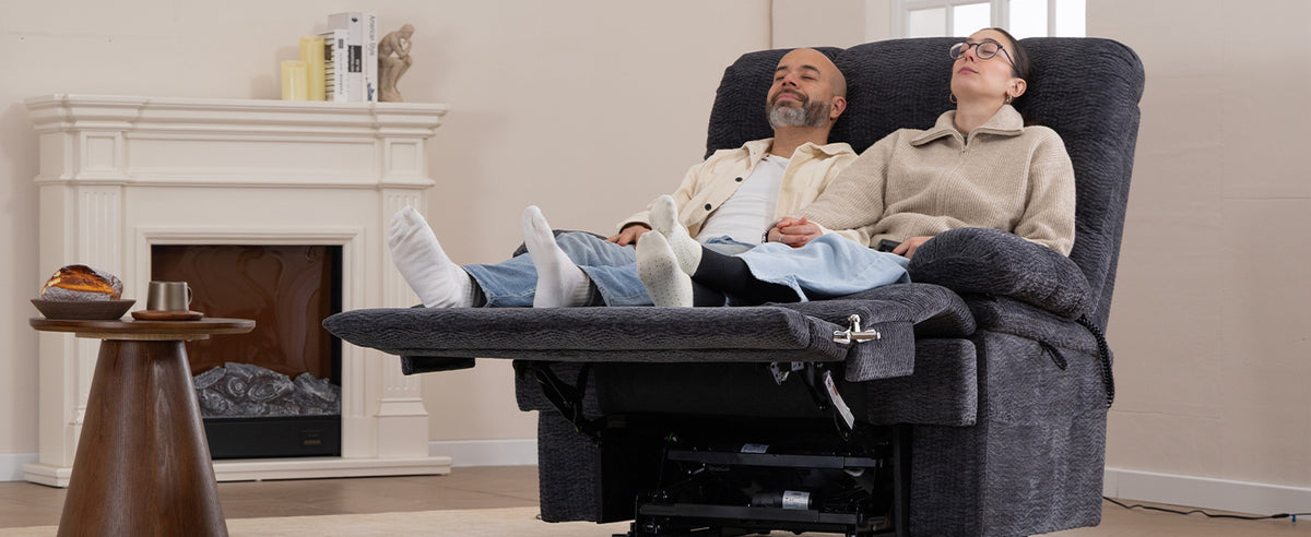 A couple resting together in one reclined Irene House 9205 EWT500 extra-wide lift recliner in front of a fireplace